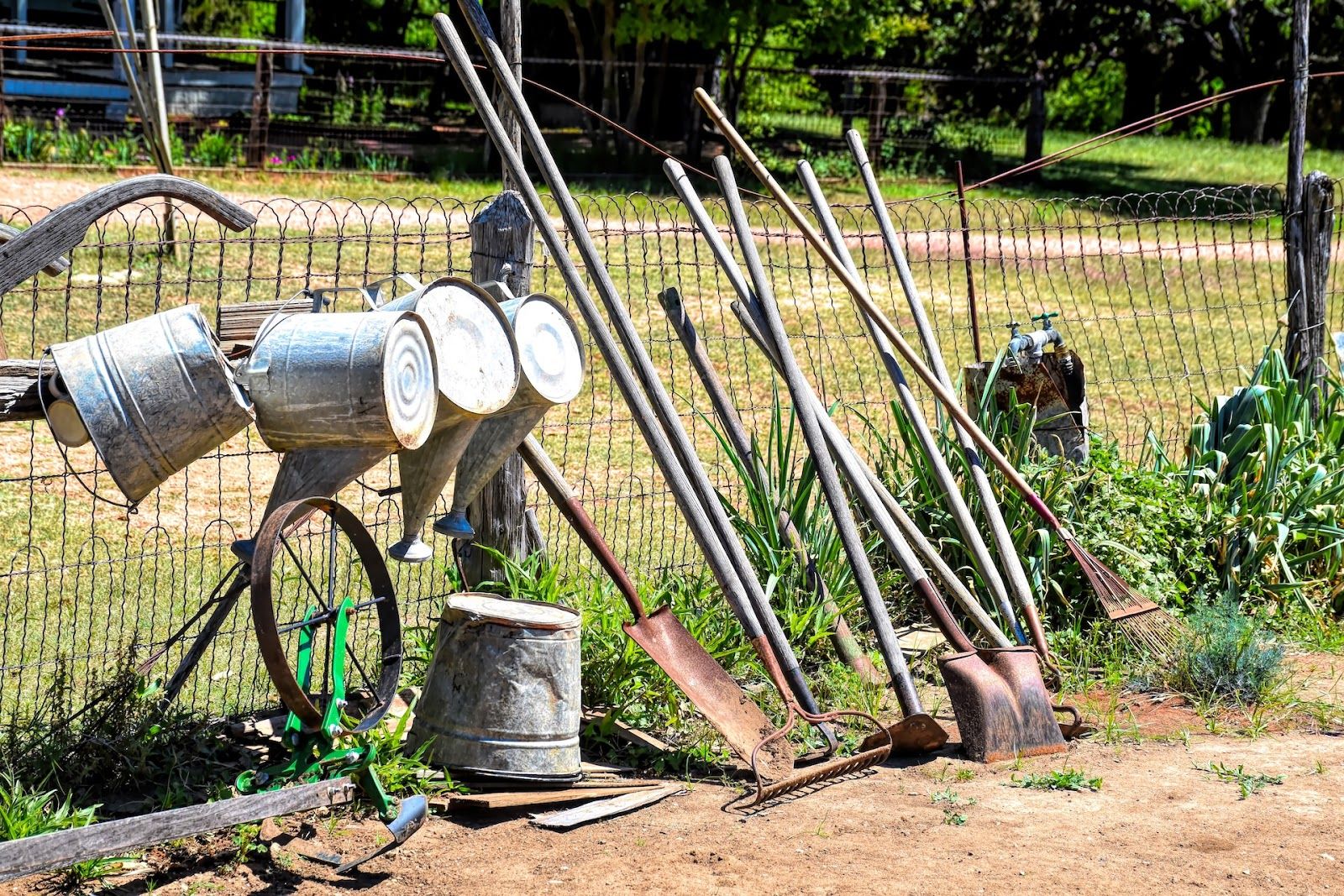 Lots of old gardening and composting equipment stacked up against a fence