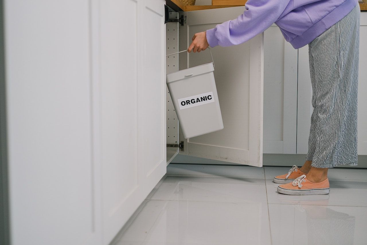 A woman puts a gray organic compost bin under the kitchen sink