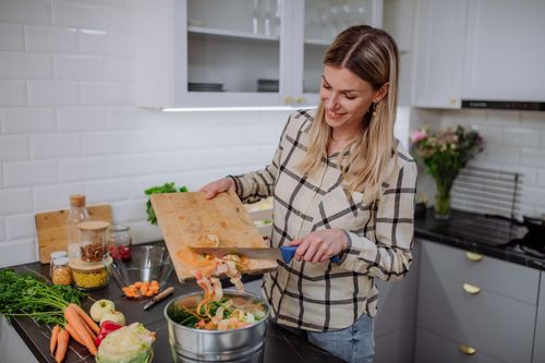 A lady scraps vegetable peelings into a compost bin in her apartment kitchen